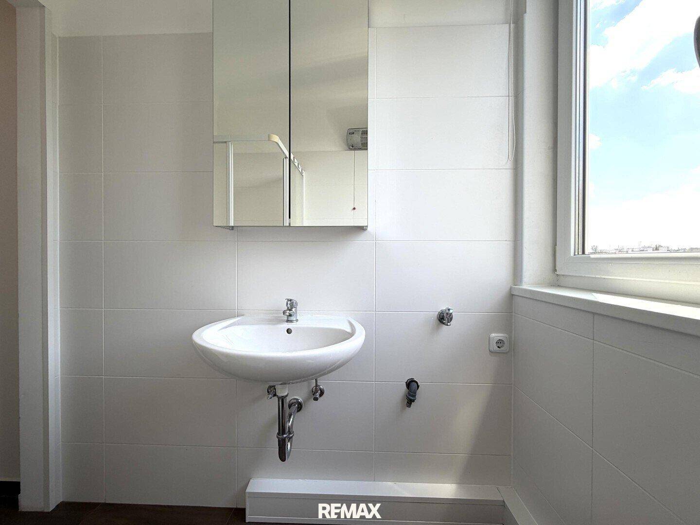 Badezimmer mit weiß gefliesten Wänden, Waschbecken und Spiegelschrank.