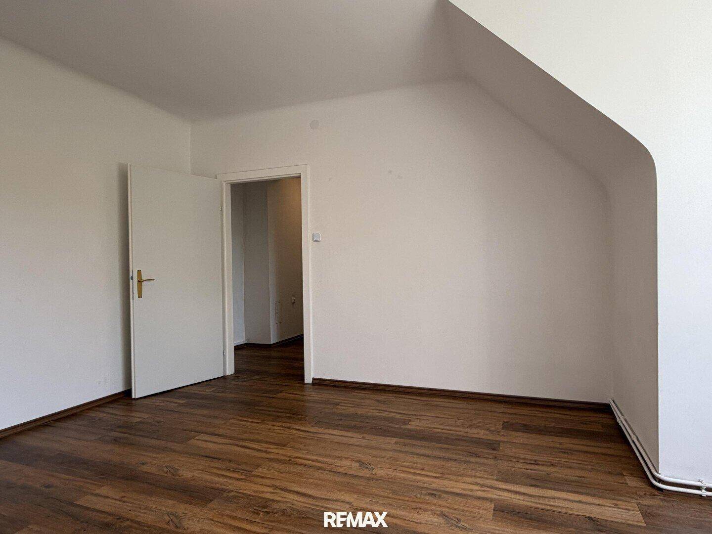 Leeres Zimmer mit Laminatboden und Zugang zu einem weiteren Bereich der Wohnung.