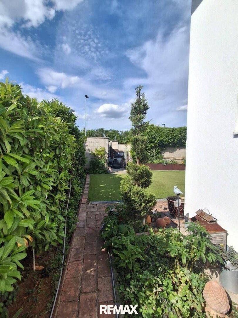 Schmaler Ziegelweg führt durch den grünen Garten mit hohen Hecken und Bäumen.