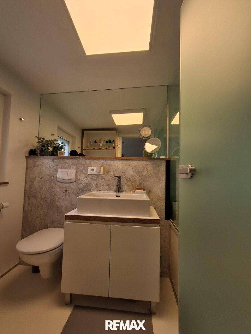 Modernes Badezimmer mit Waschtisch, WC und großem Spiegel, der den Raum erweitert.