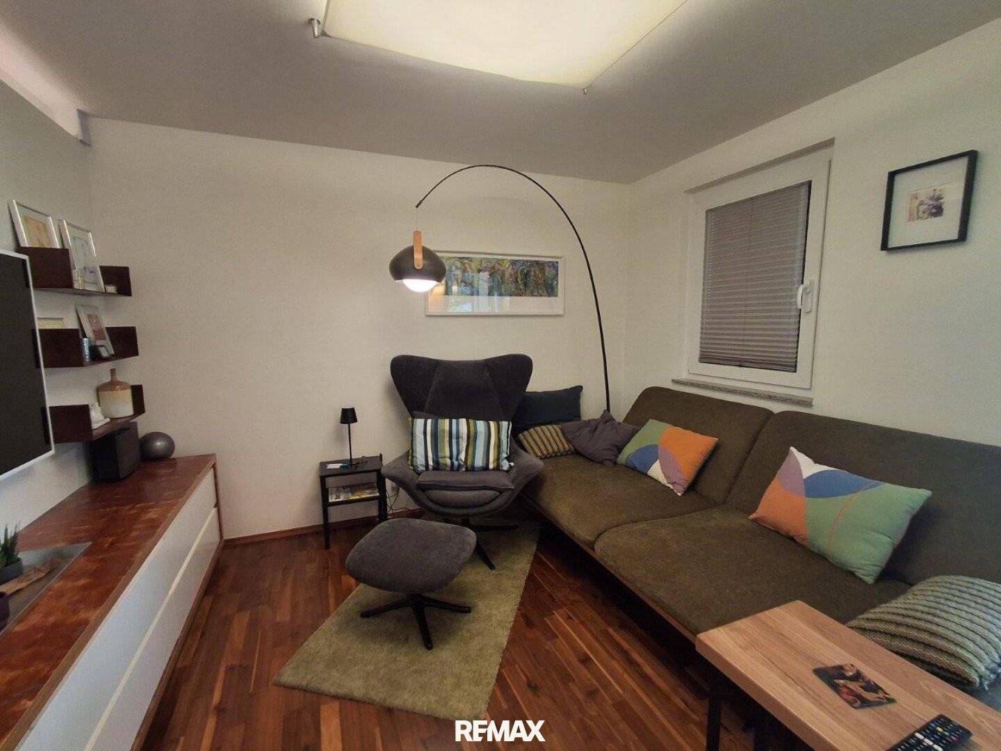 Gemütliches Wohnzimmer mit bequemer Sitzecke, Stehlampe und Holzboden.