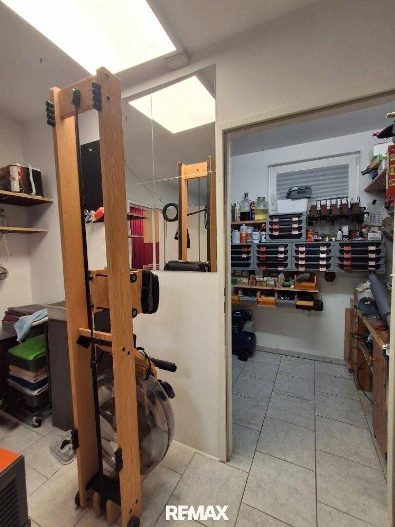 Fitnessraum mit Rudergerät und angrenzendem Werkstattbereich mit Regalen.