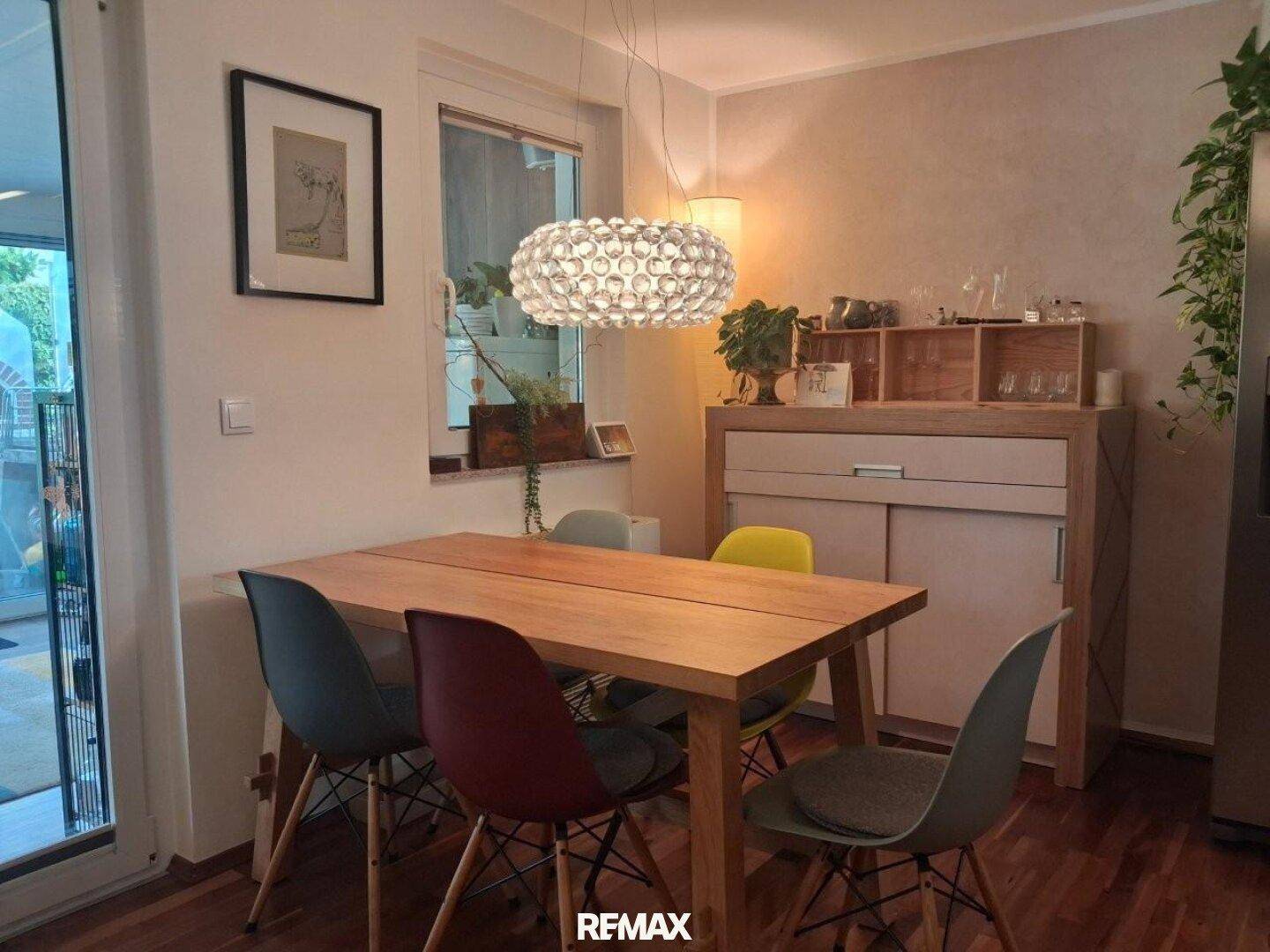 Heller Essbereich mit Holztisch, farbigen Stühlen und modernem Deckenlicht.