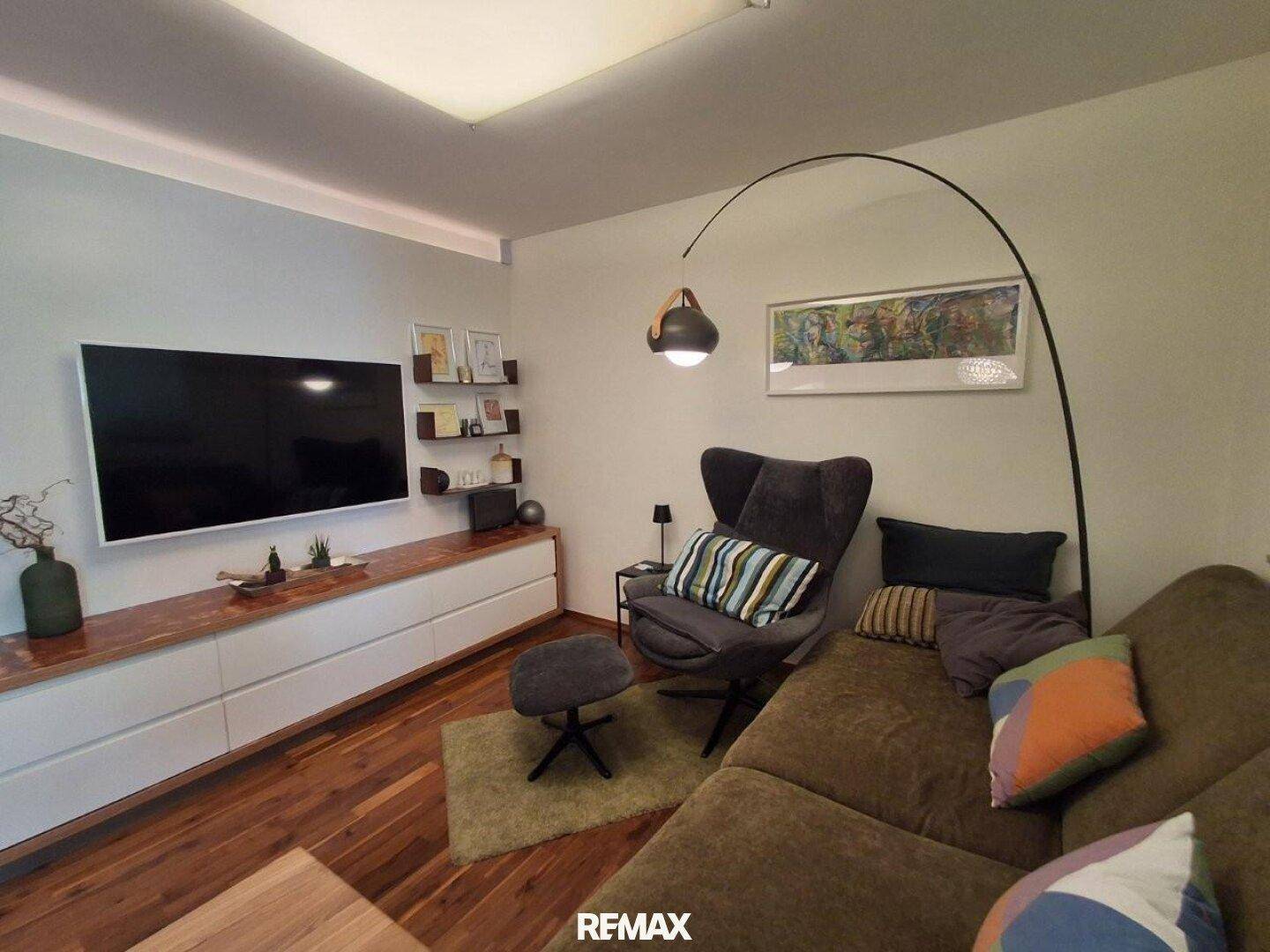 Gemütliches Wohnzimmer mit großem Fernseher, bequemer Couch und Holzboden.