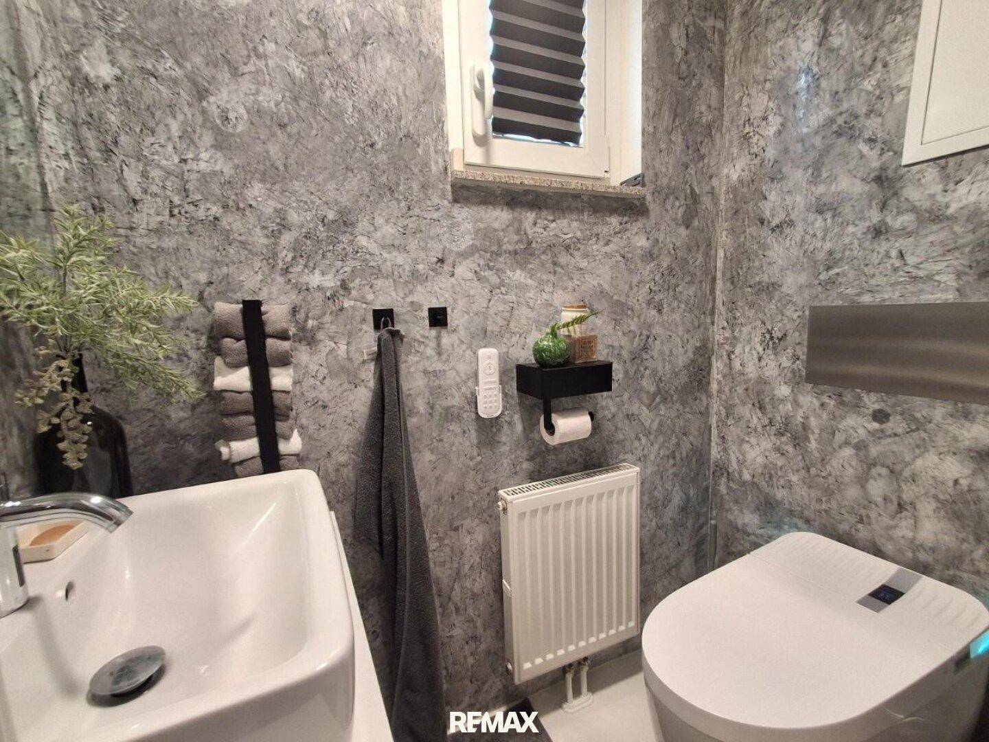 Modernes Gäste-WC mit Waschbecken, wandhängendem WC und strukturierten grauen Wänden.