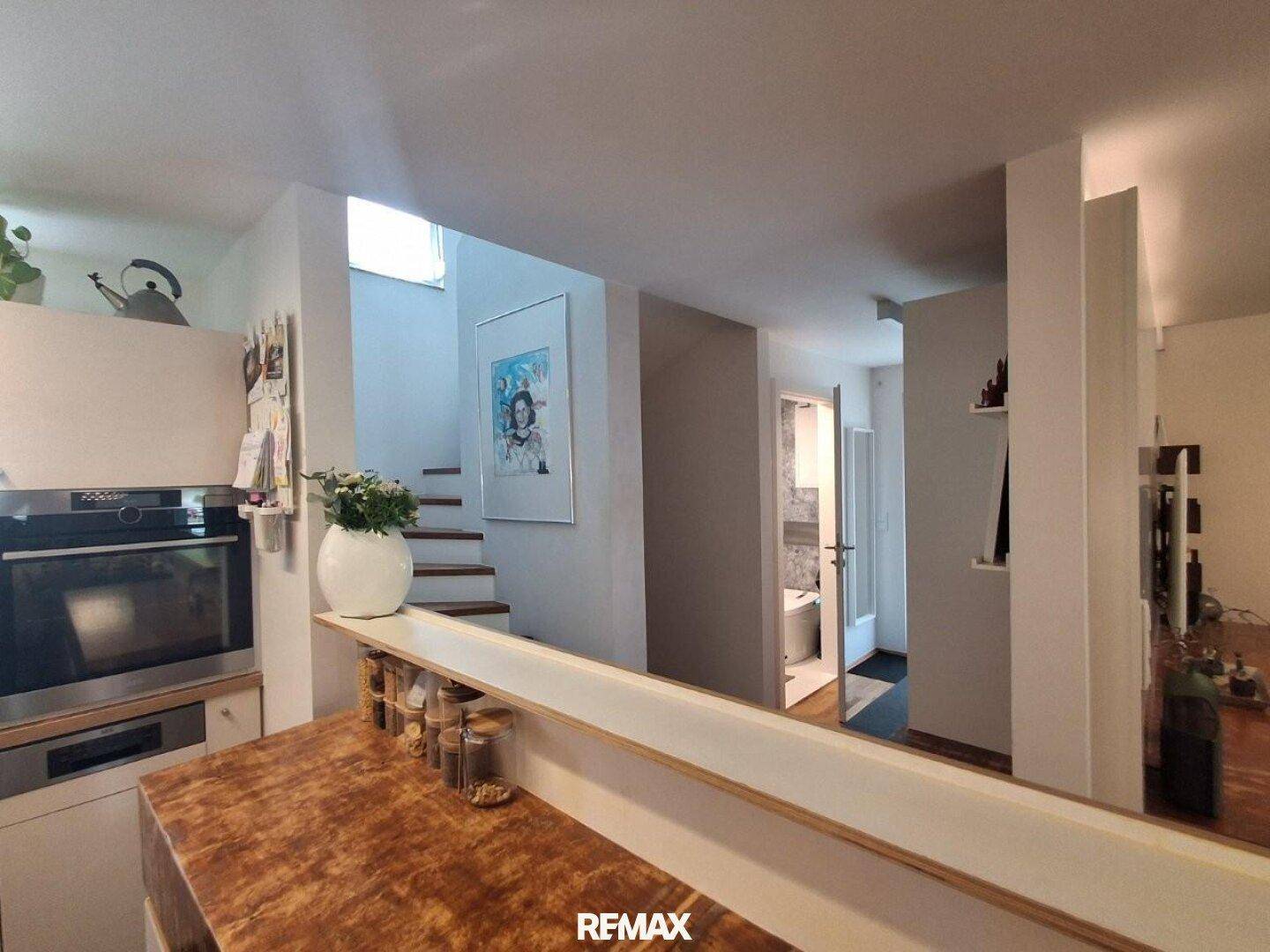 Offener Übergang von der Küche zum Flur mit Holztreppe und Blick ins Badezimmer.