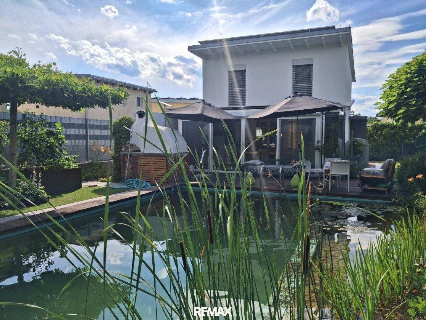 Rückansicht des Hauses mit großem Schwimmteich, Holzterrasse und Sonnenschirmen.