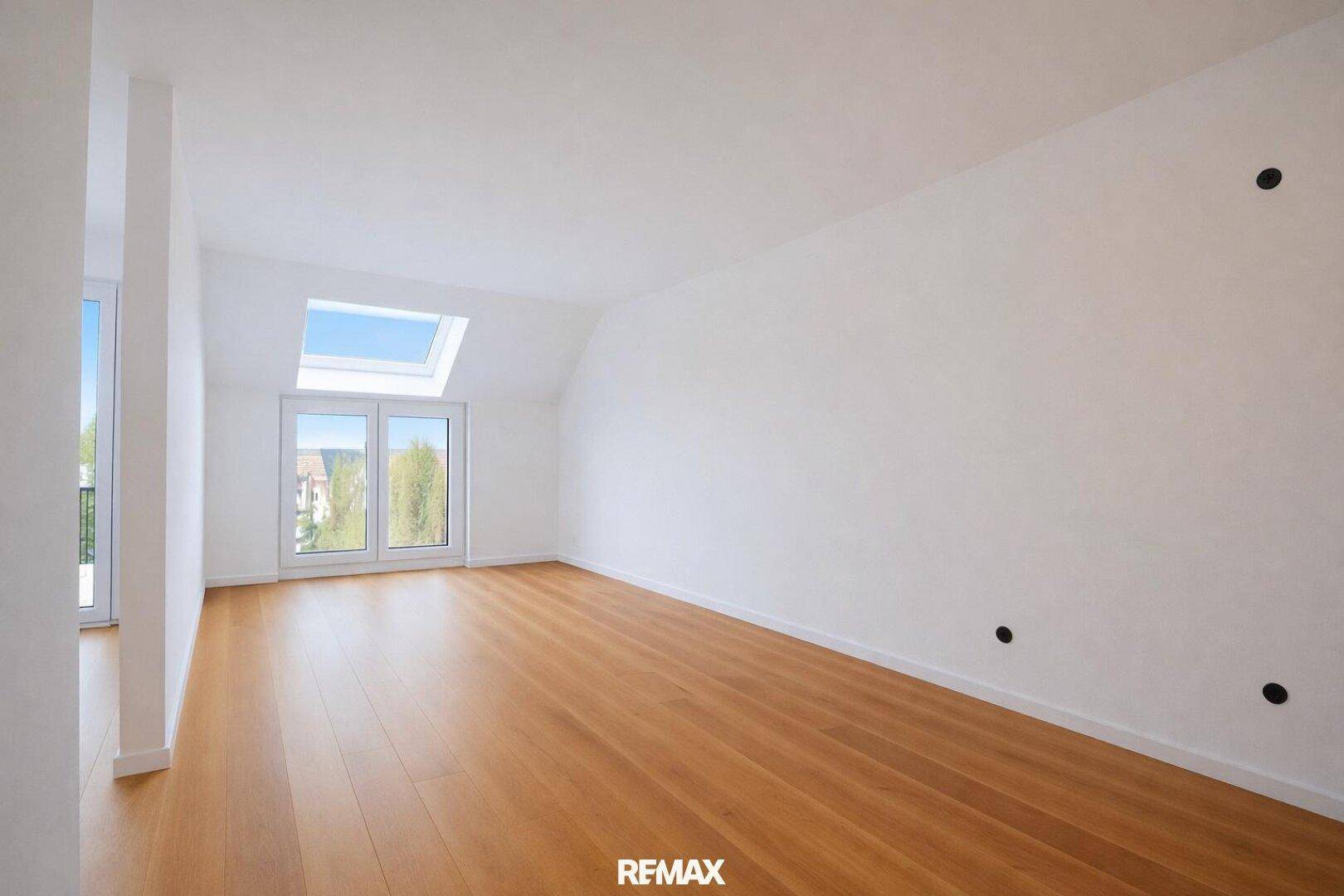 Heller, leerer Wohnraum mit Holzboden, Dachfenster und Zugang zu einem Balkon.