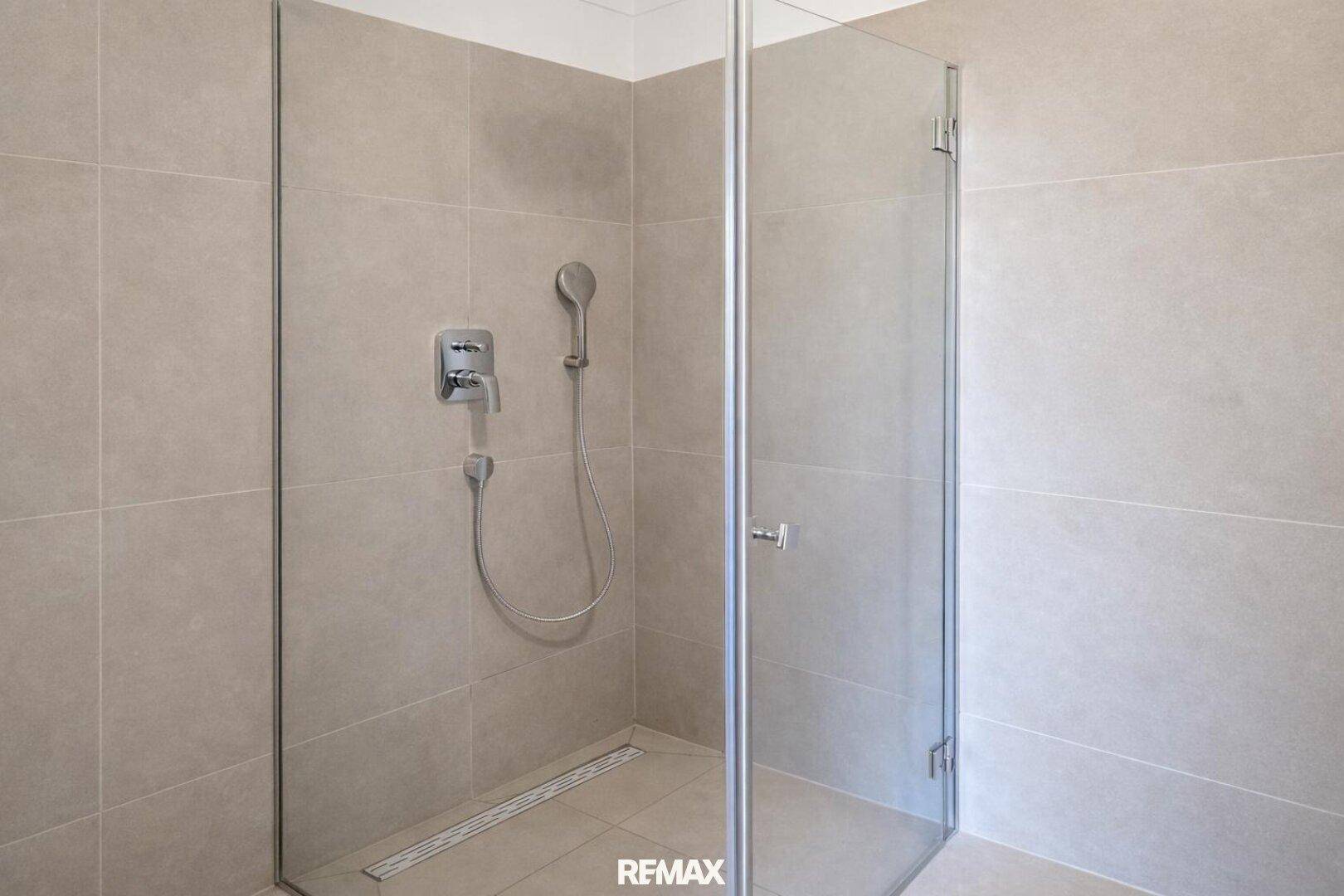Geräumige Dusche mit Glasabtrennung und modernen grauen Fliesen im Badezimmer.