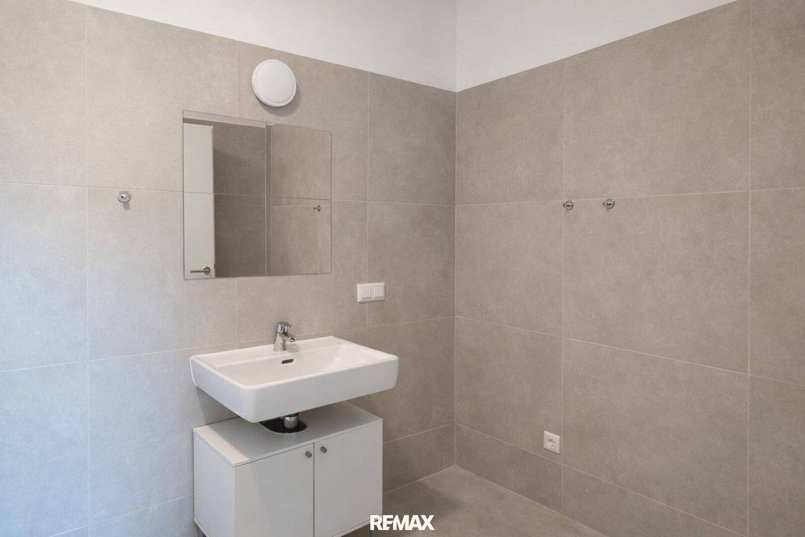 Modernes Badezimmer mit grauen Fliesen, Einzelwaschbecken und Spiegel über dem Waschtisch.