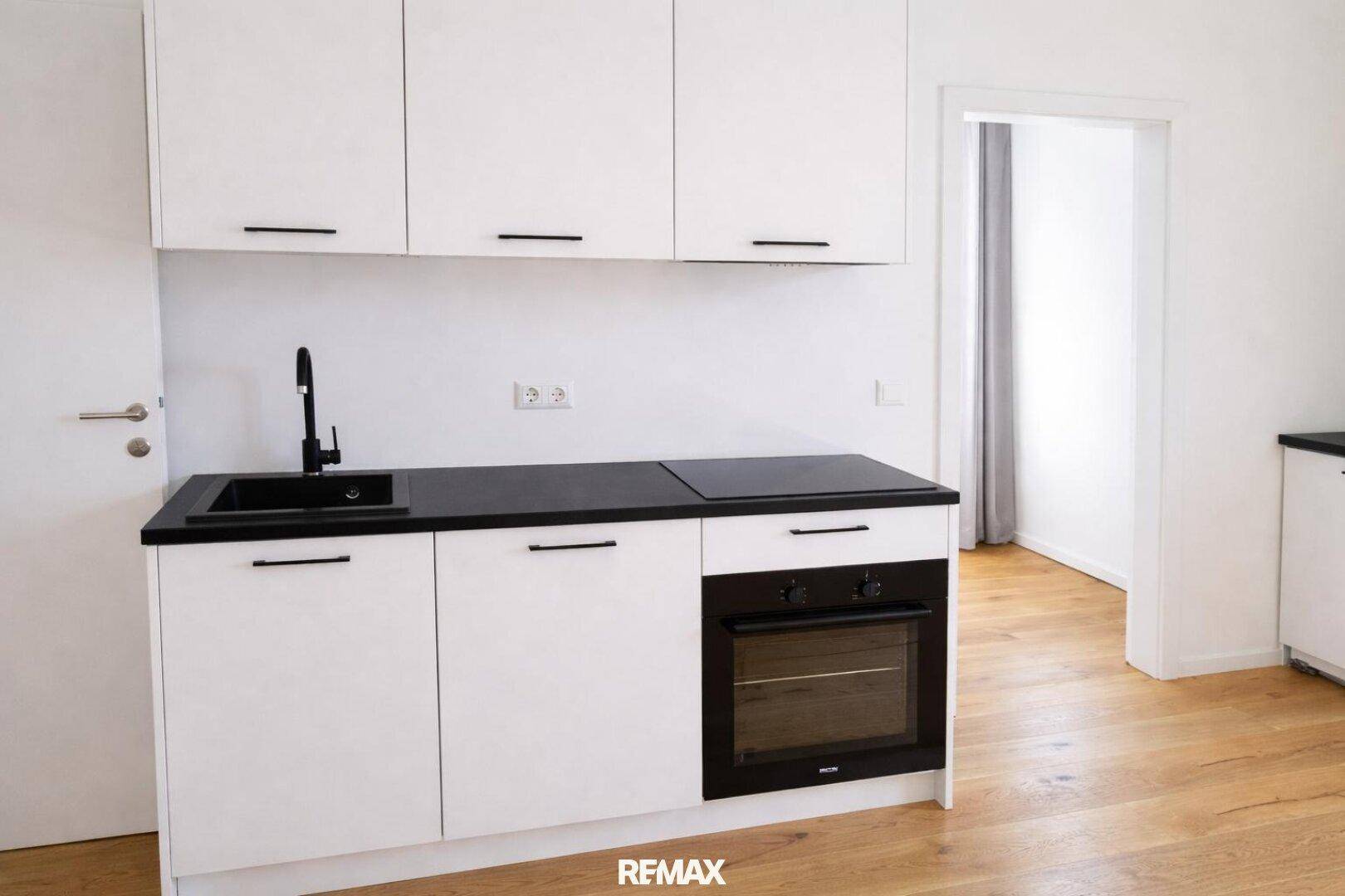 Moderne Küchenzeile mit weißen Schränken, schwarzer Arbeitsplatte und integriertem Backofen.