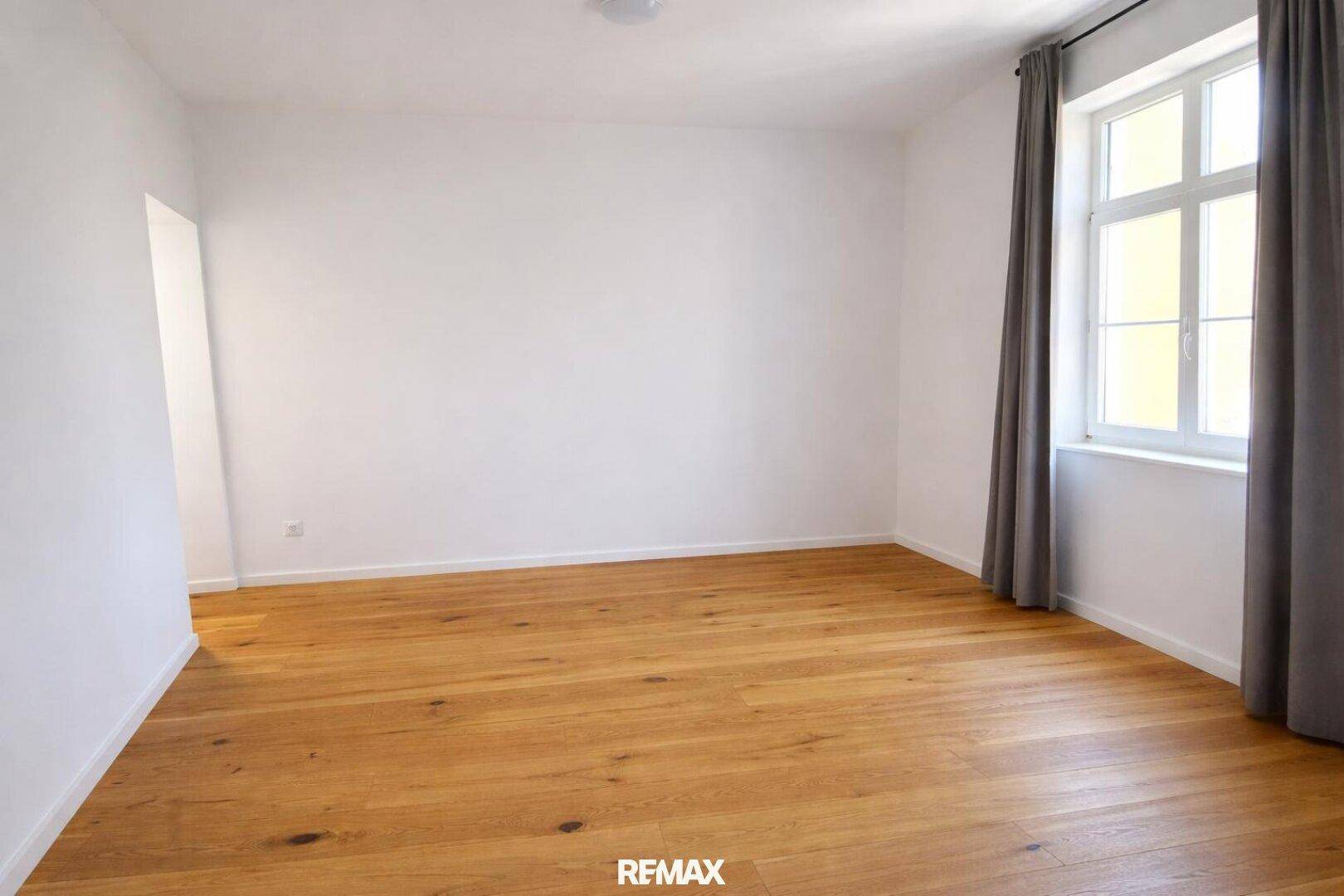 Helles, leeres Zimmer mit Holzboden und großem Fenster, bereit zur individuellen Gestaltung.