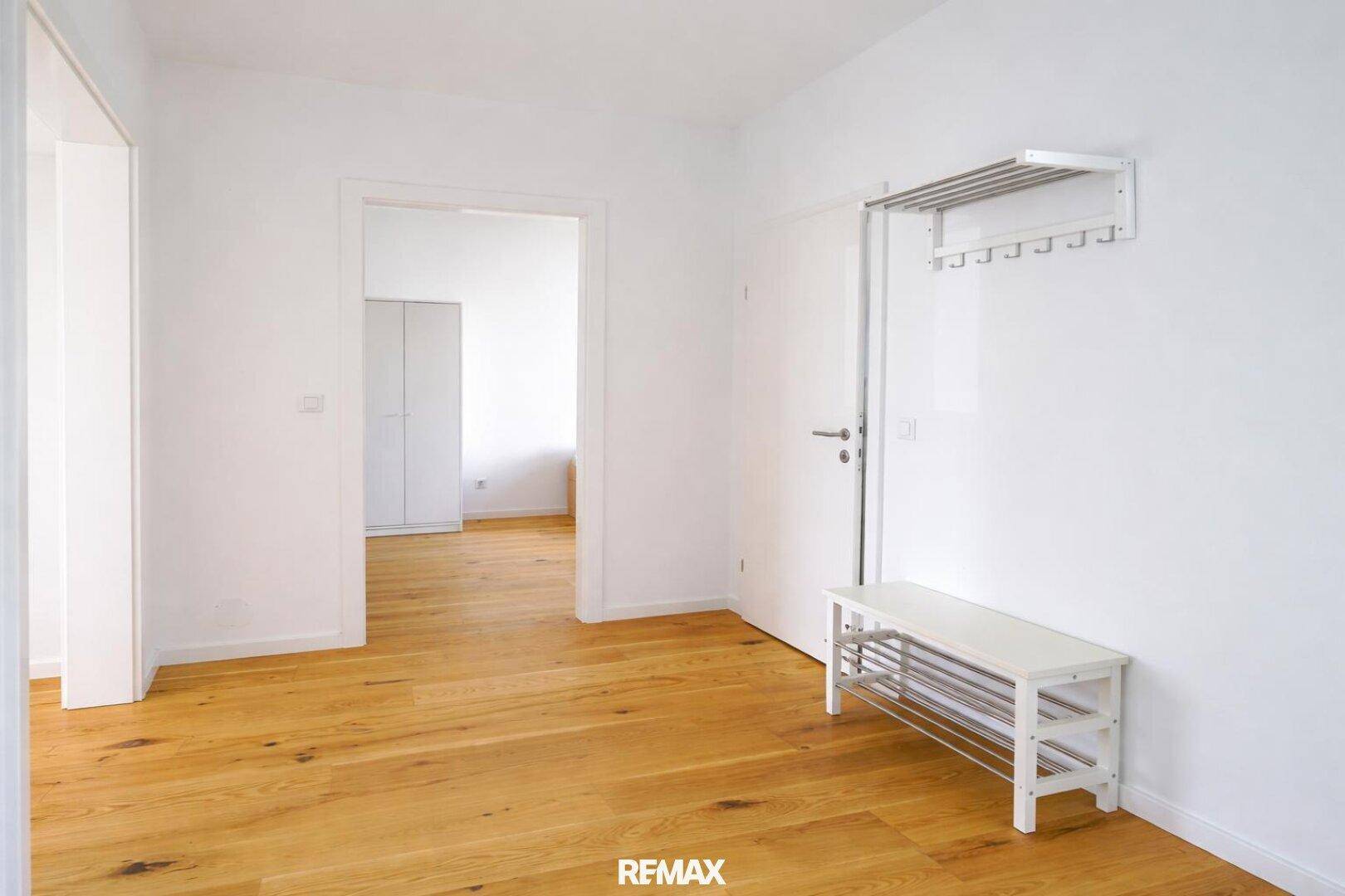 Heller Flur mit Holzboden und einfacher Garderobe, der zu weiteren Räumen führt.