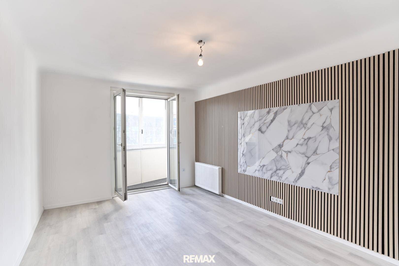 Modernes Zimmer mit Holzlattung, Marmor-Akzentwand und Zugang zu einem verglasten Balkon.