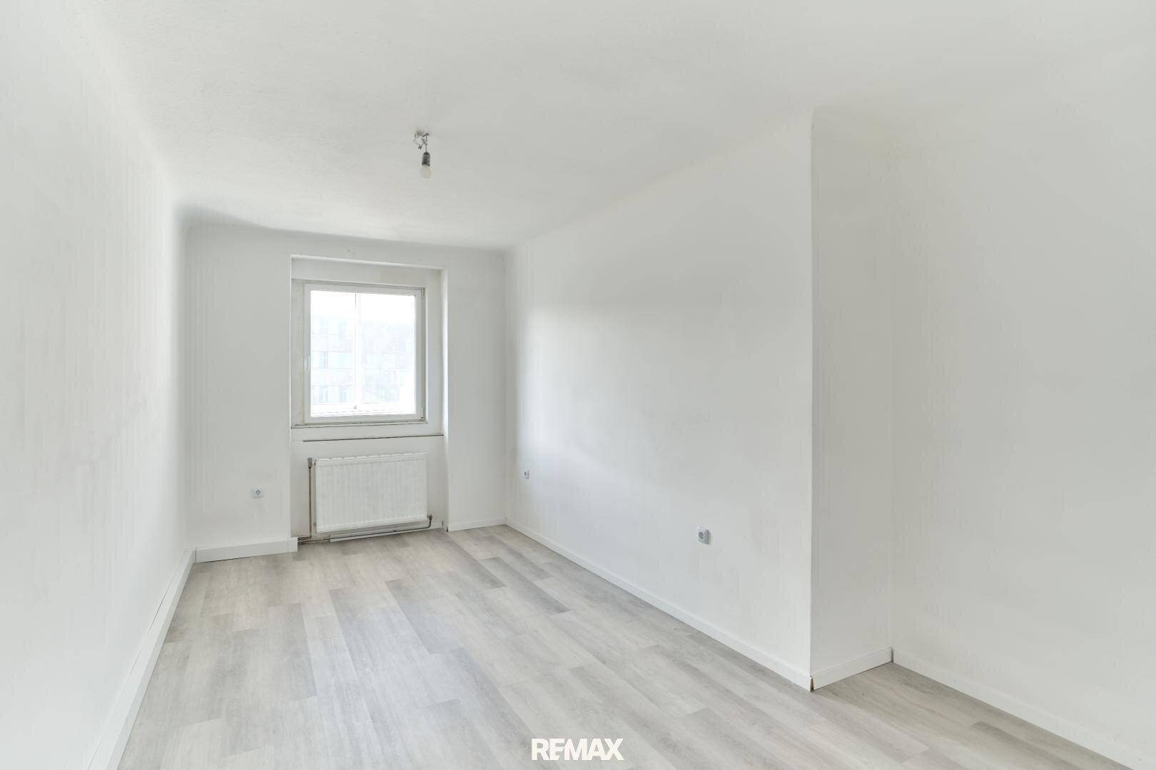 Helles Schlafzimmer mit Laminatboden und einem Fenster, das viel Licht hereinlässt.