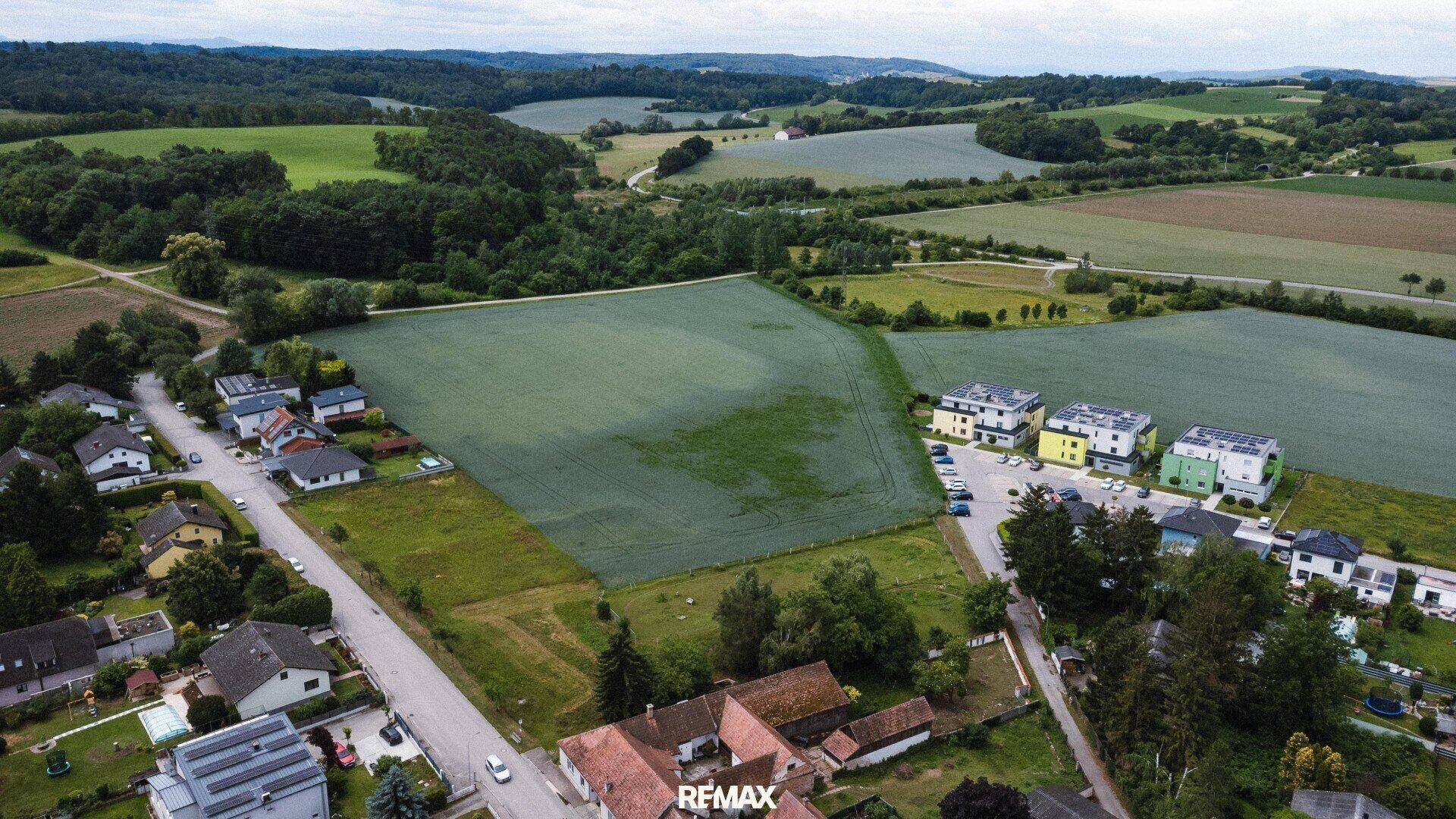 Weitläufige Luftaufnahme einer ländlichen Siedlung mit Feldern und bewaldeten Hügeln.