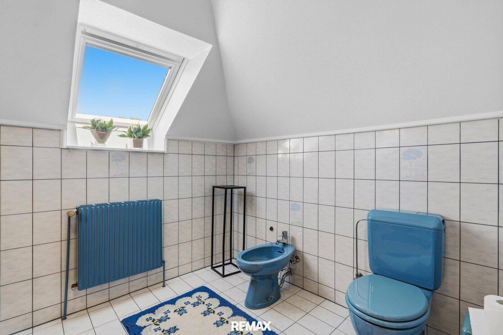 Badezimmer im Dachgeschoss mit blauen Sanitärobjekten, weißen Fliesen und Dachfenster.