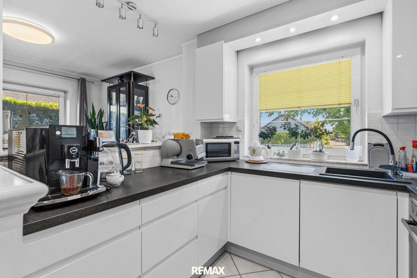 Moderne Küche mit weißen Schränken, dunkler Arbeitsplatte und Fenster mit Blick ins Grüne.