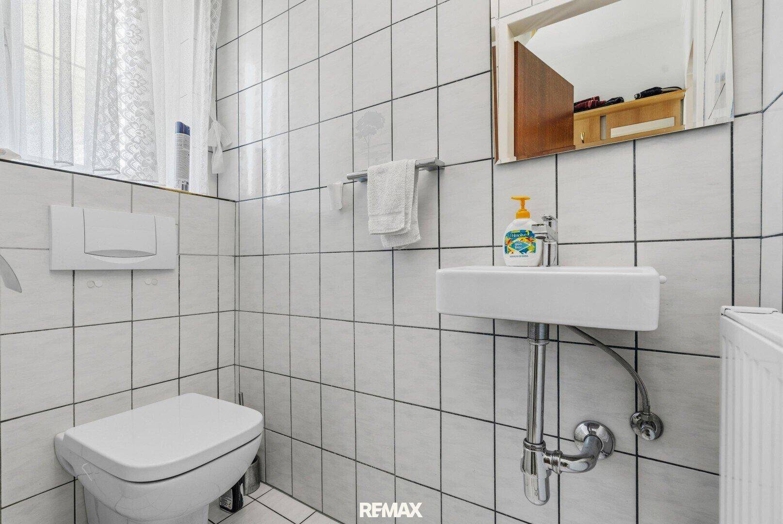 Kleines Gäste-WC mit weißen Fliesen, wandhängendem WC und Handwaschbecken.