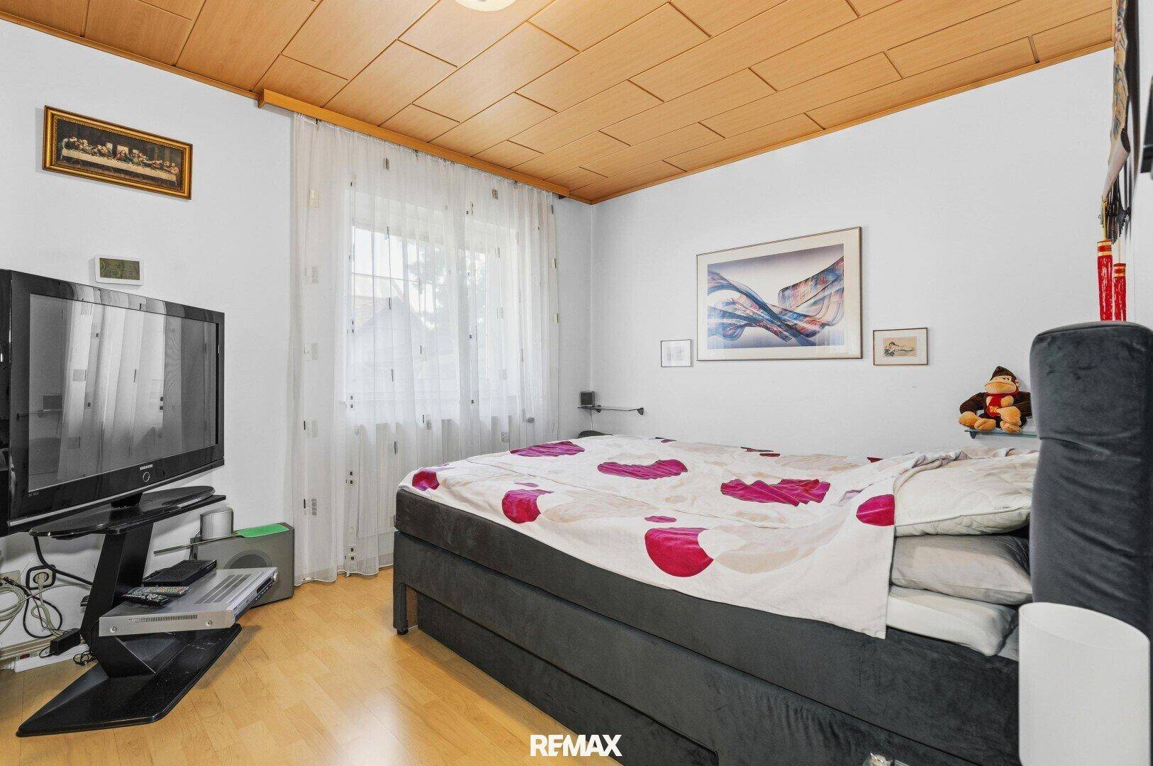 Schlafzimmer mit Holzbalkendecke, Doppelbett und Fernseher, hell und gemütlich.