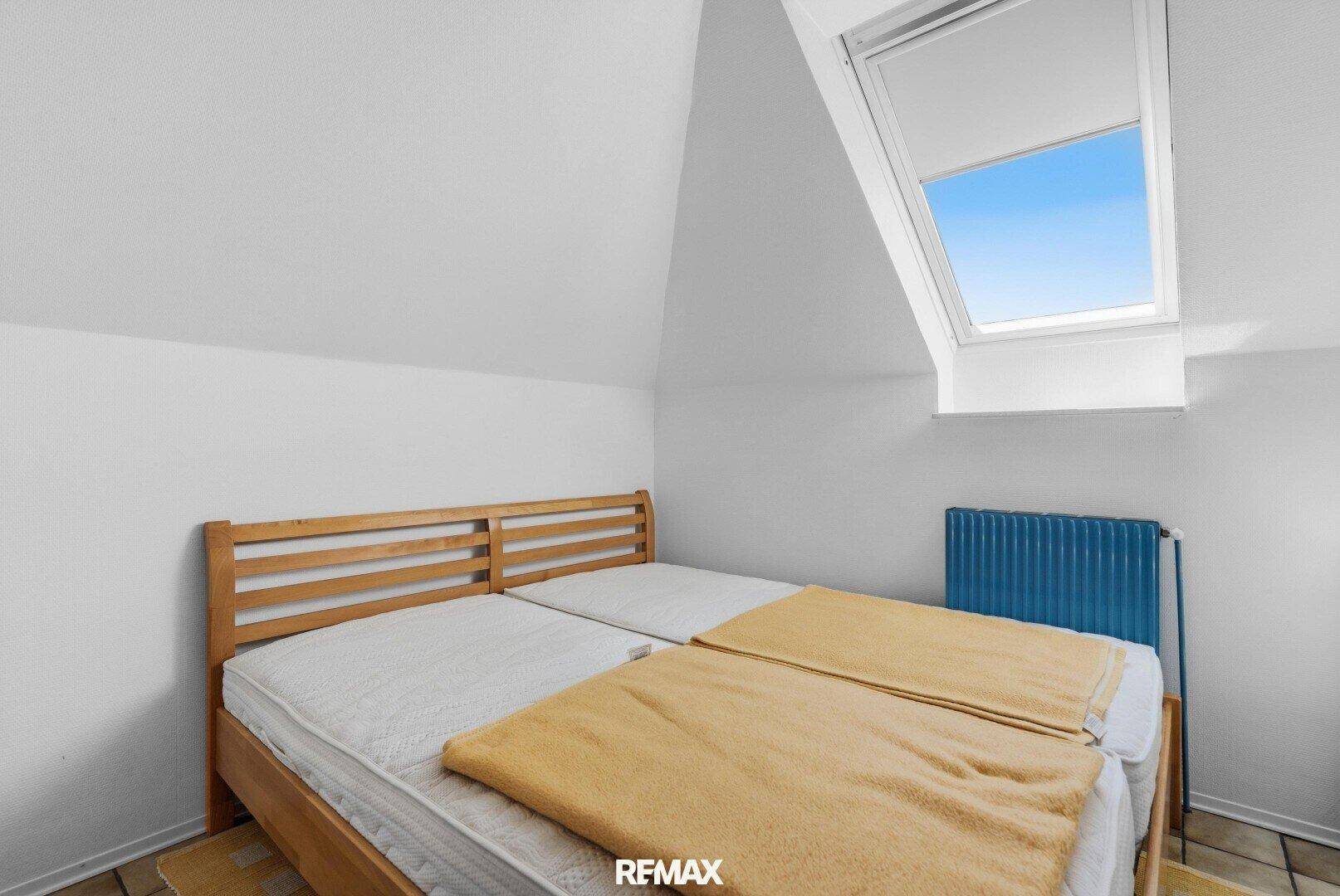 Dachschlafzimmer mit zwei Einzelbetten, Holzbettrahmen und Dachfenster für Tageslicht.