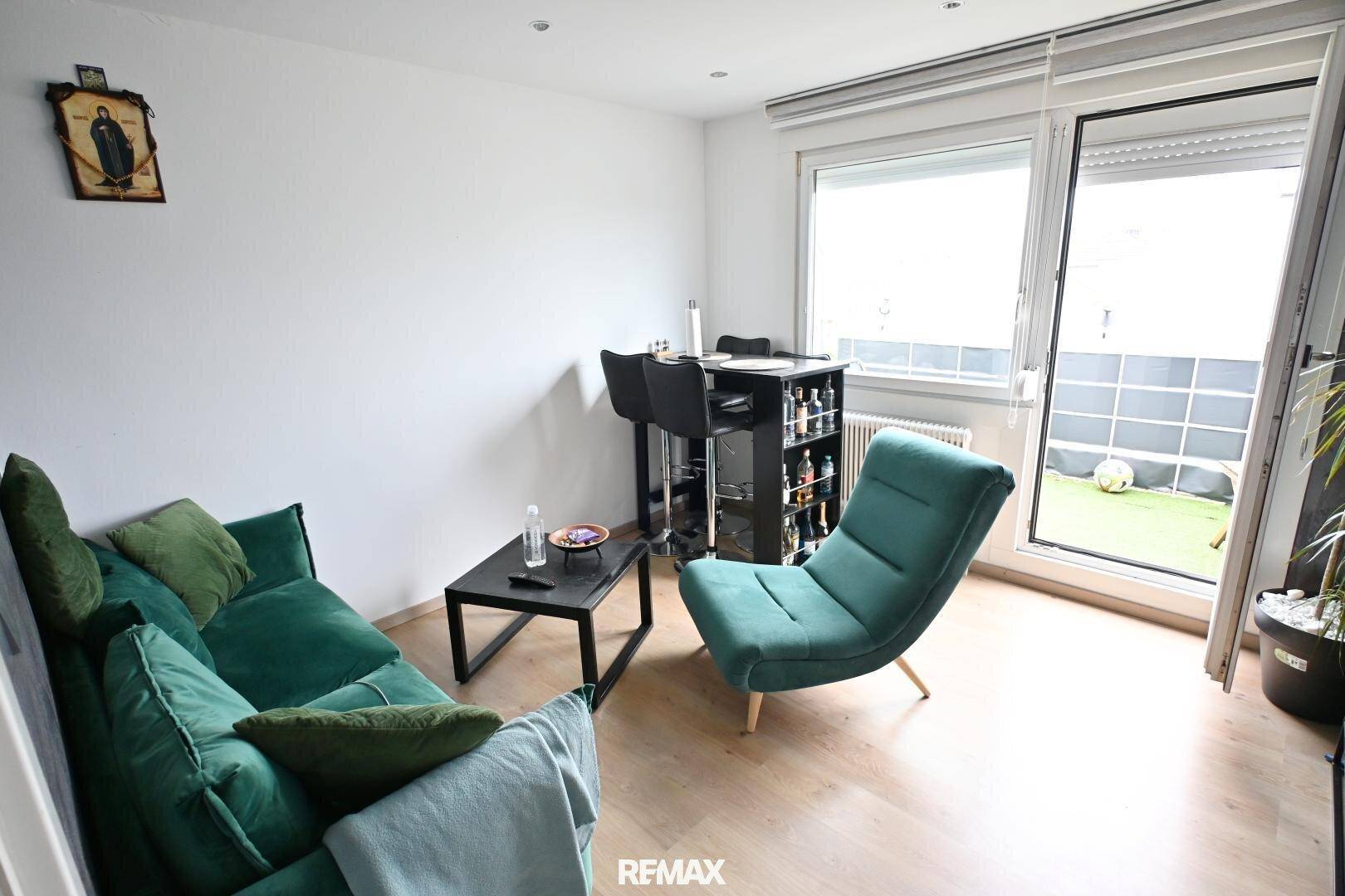 Helles Wohnzimmer mit modernem Sofa, Sessel und Zugang zum Balkon.