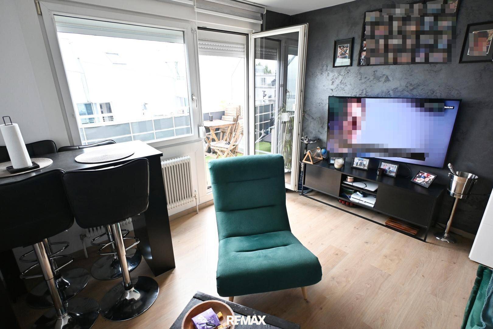 Modern eingerichtetes Wohnzimmer mit Fernseher, Barhockern und Balkonzugang.
