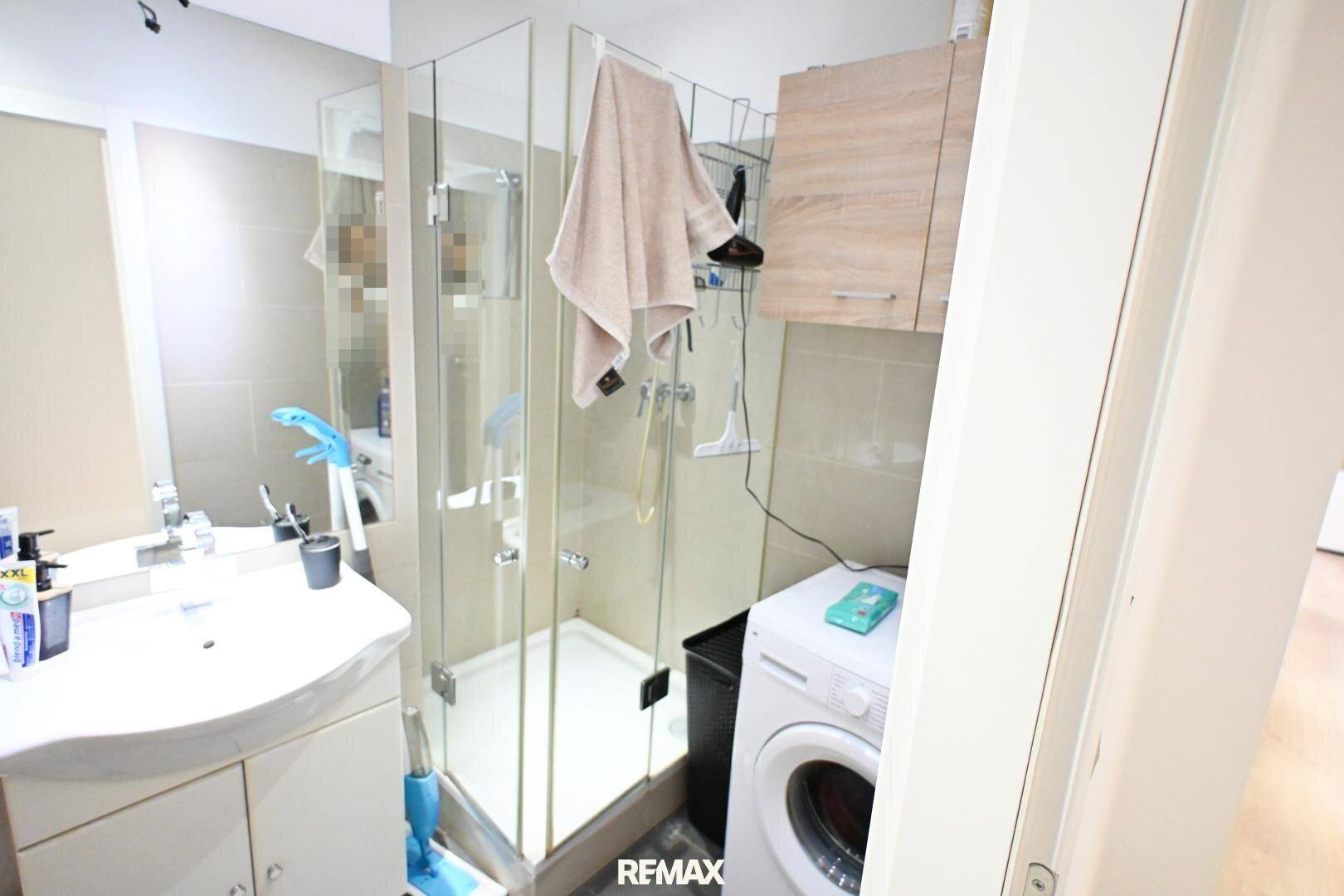 Modernes Badezimmer mit Dusche, Waschmaschine und Waschbecken, praktisch eingerichtet.