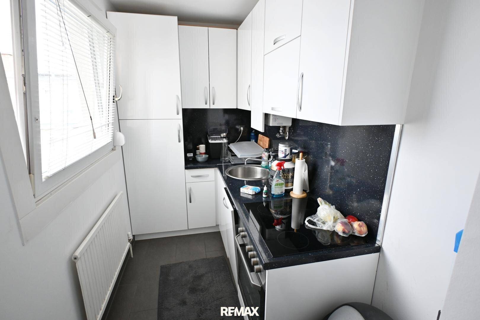 Kleine, funktionale Küche mit weißen Schränken, dunkler Arbeitsplatte und Fenster.