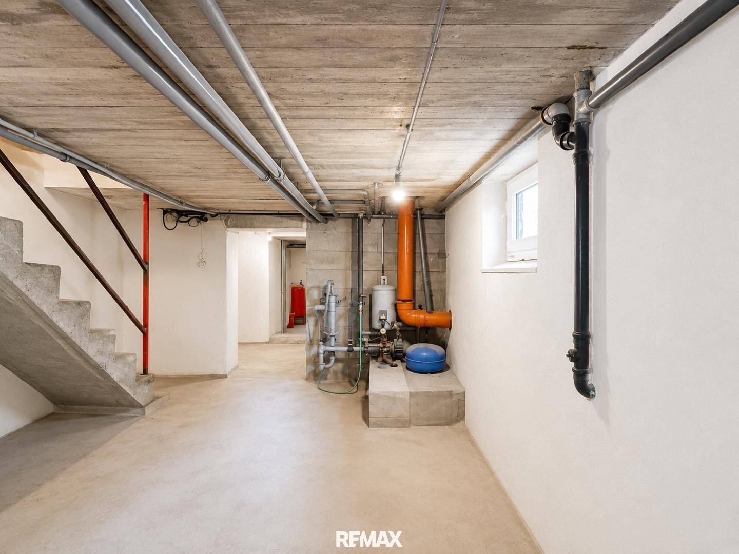 Kellerflur mit Treppenzugang und sichtbaren Versorgungsleitungen, funktional gestaltet.