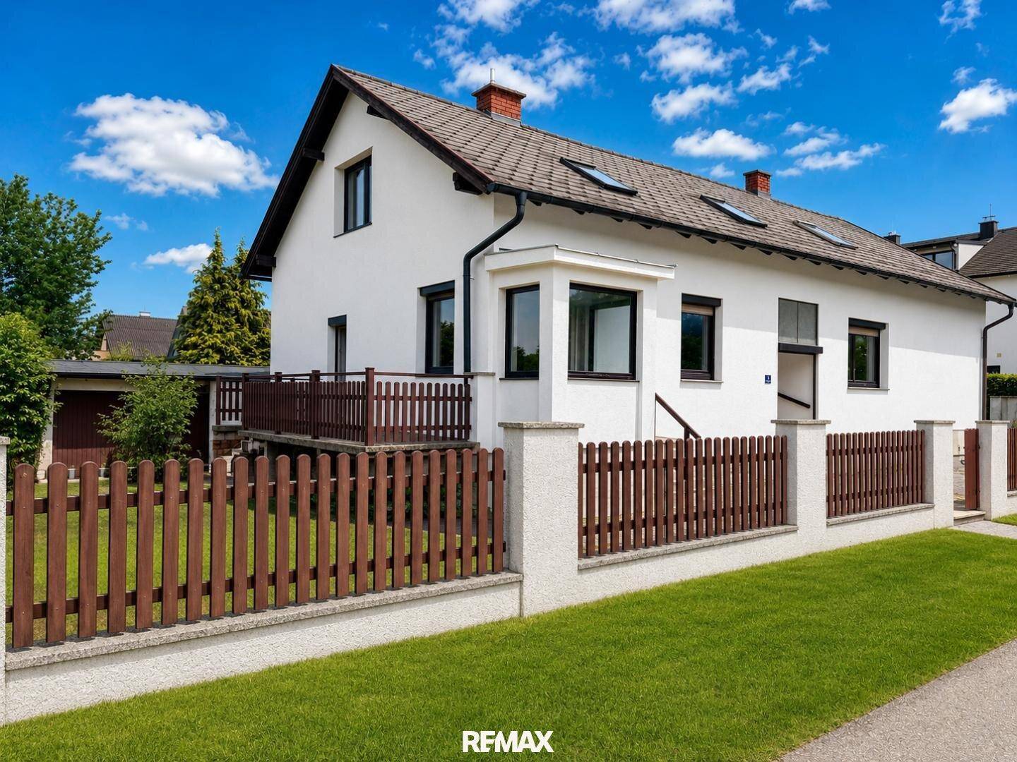 Seitenansicht des Hauses mit braunem Holzzaun, gepflegtem Vorgarten und Dachfenstern.