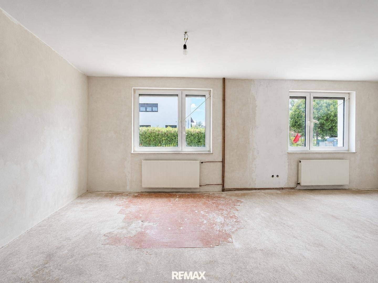 Geräumiger Raum in Renovierung mit zwei Fenstern und unfertigem Bodenbelag.