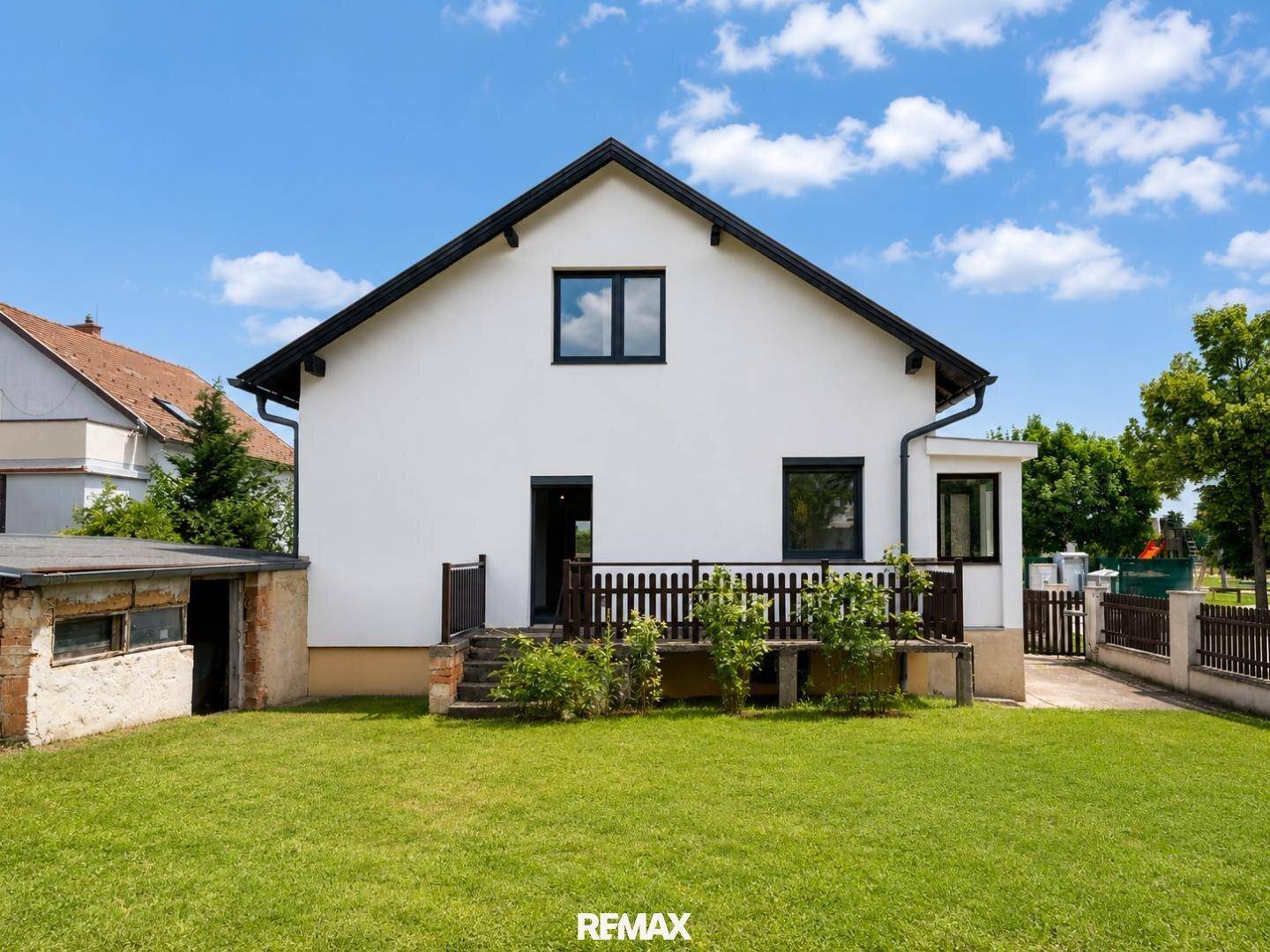 Rückansicht des Hauses mit Terrasse und gepflegtem Rasen unter blauem Himmel.