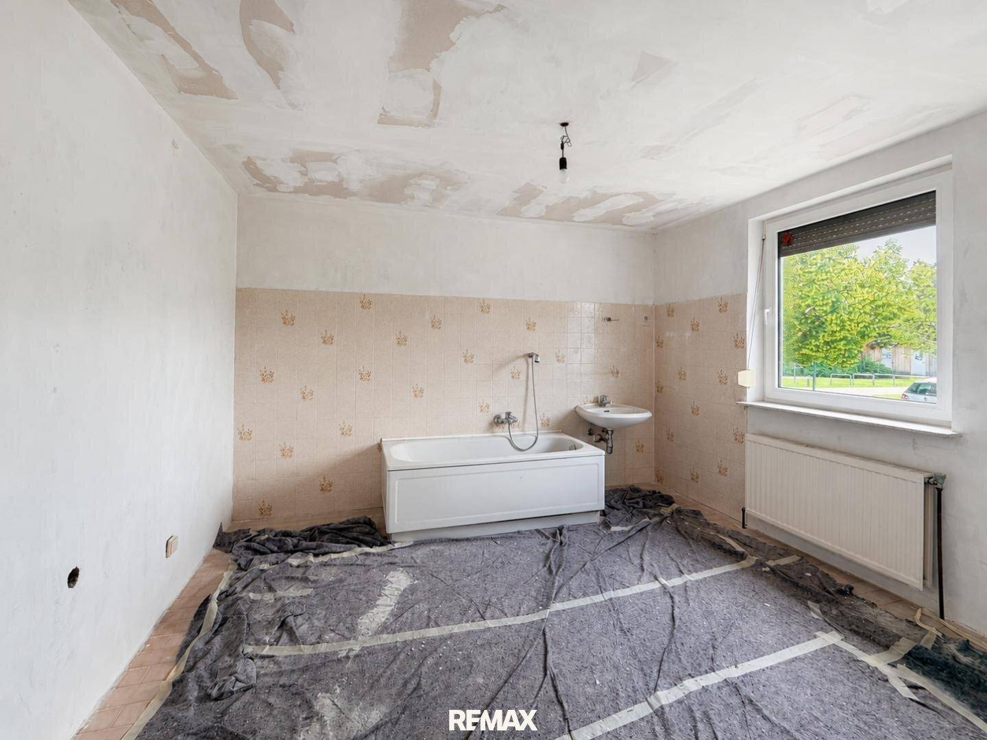 Badezimmer in Renovierung mit Badewanne, Waschbecken und älteren Wandfliesen.