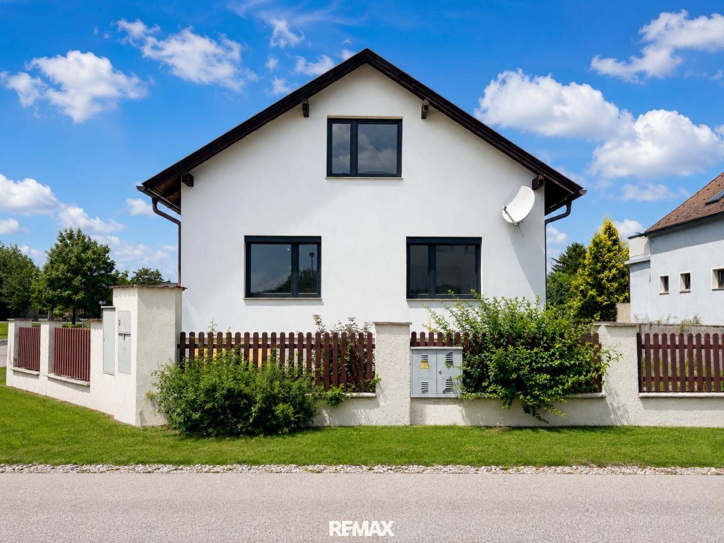 Vorderansicht des Hauses mit weißer Fassade, dunklen Fenstern und einem gepflegten Vorgarten.