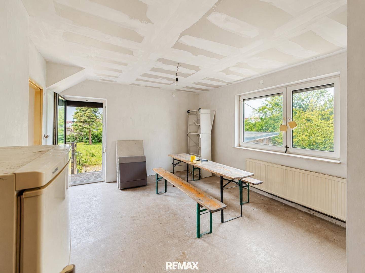 Renovierungsbedürftiger Raum mit provisorischen Bänken, Tisch und Blick in den Garten.