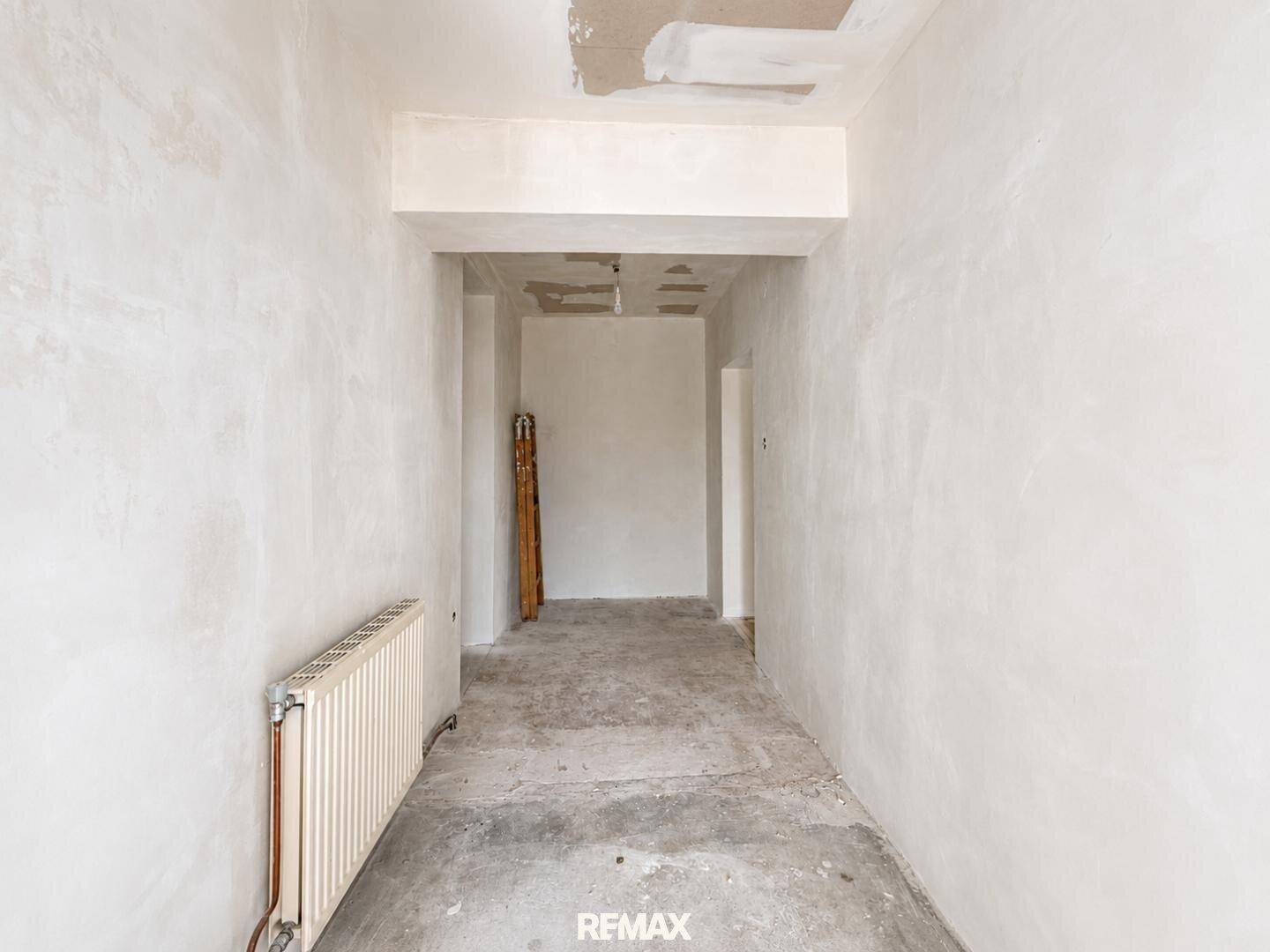 Langer, heller Flur mit Heizkörper und unfertigem Boden, bereit für die Renovierung.