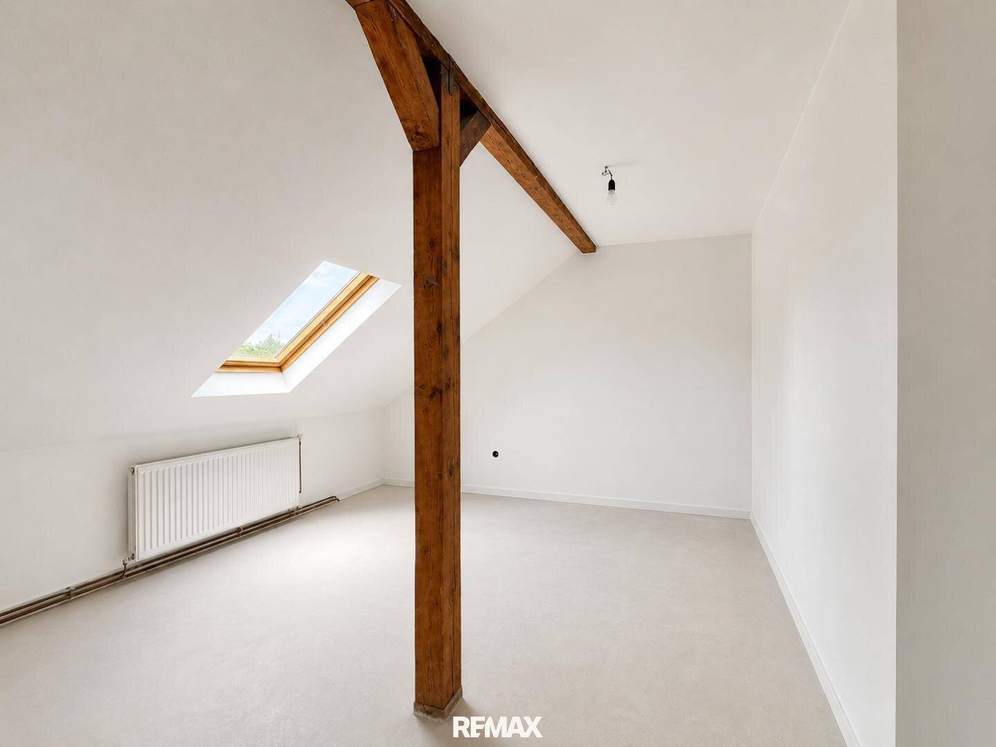 Helles Dachgeschosszimmer mit sichtbarem Holzbalken und Dachfenster, bereit für den Ausbau.
