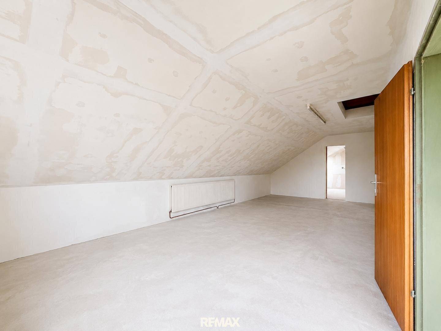 Unfertiger Dachbodenraum mit schräger Decke und Heizkörper, bereit für den Ausbau.