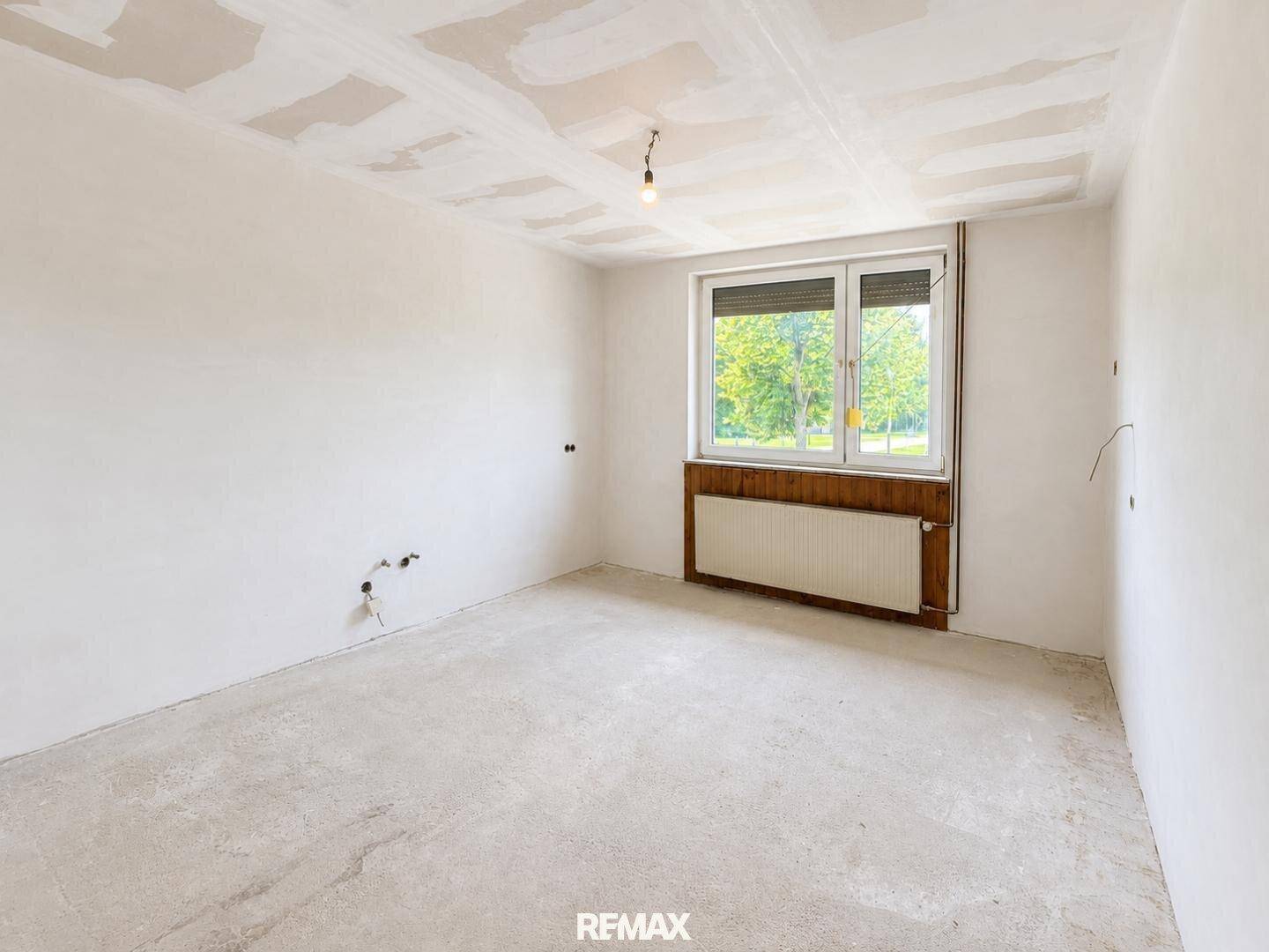 Renovierungsbedürftiger Raum mit großem Fenster und Heizkörper, bereit für die Gestaltung.