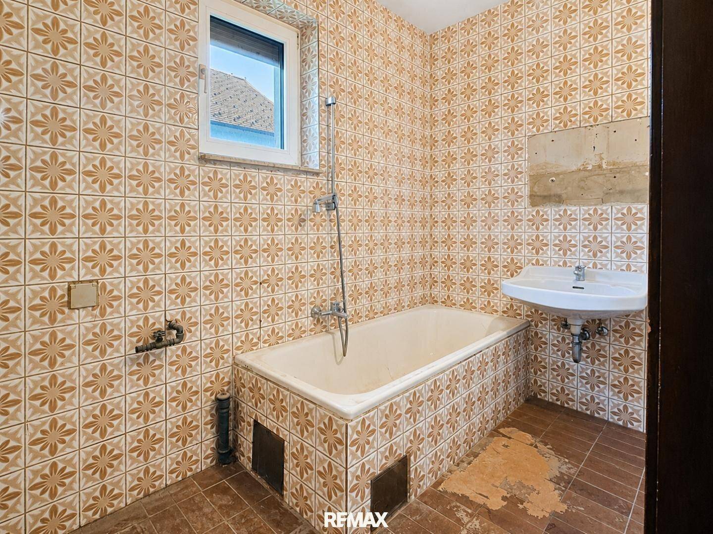 Badezimmer mit älteren Fliesen, Badewanne und Waschbecken, das eine Modernisierung benötigt.