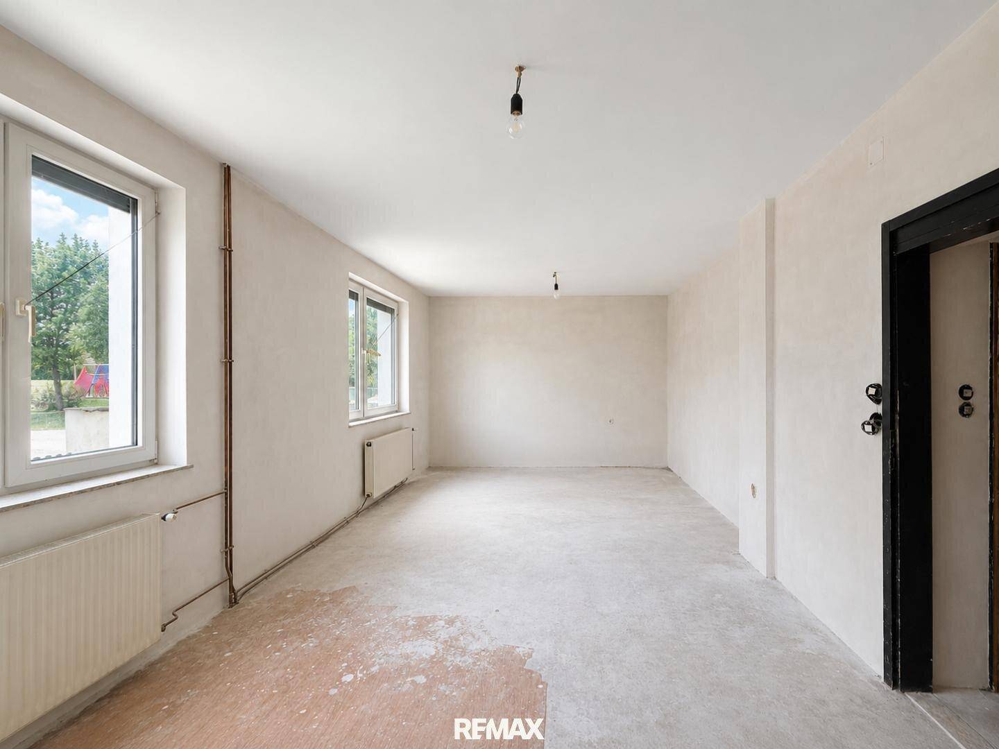 Geräumiger Raum in Renovierung mit zwei Fenstern und unfertigem Bodenbelag.