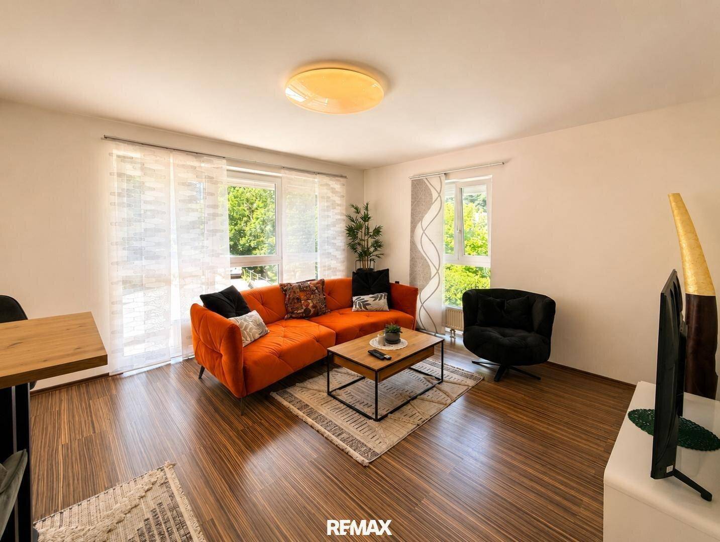 Helles Wohnzimmer mit großzügigen Fenstern, orangefarbenem Sofa und Holzboden.