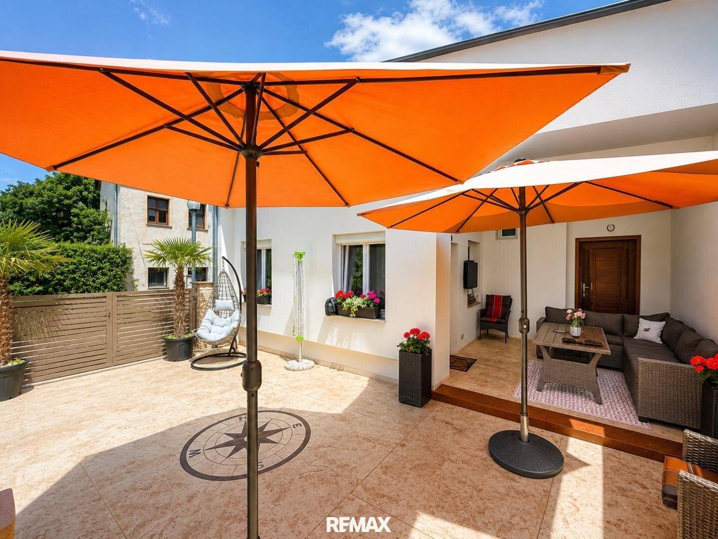 Große Terrasse mit Sonnenschirmen, bequemen Sitzgelegenheiten und Pflanzen in Töpfen.