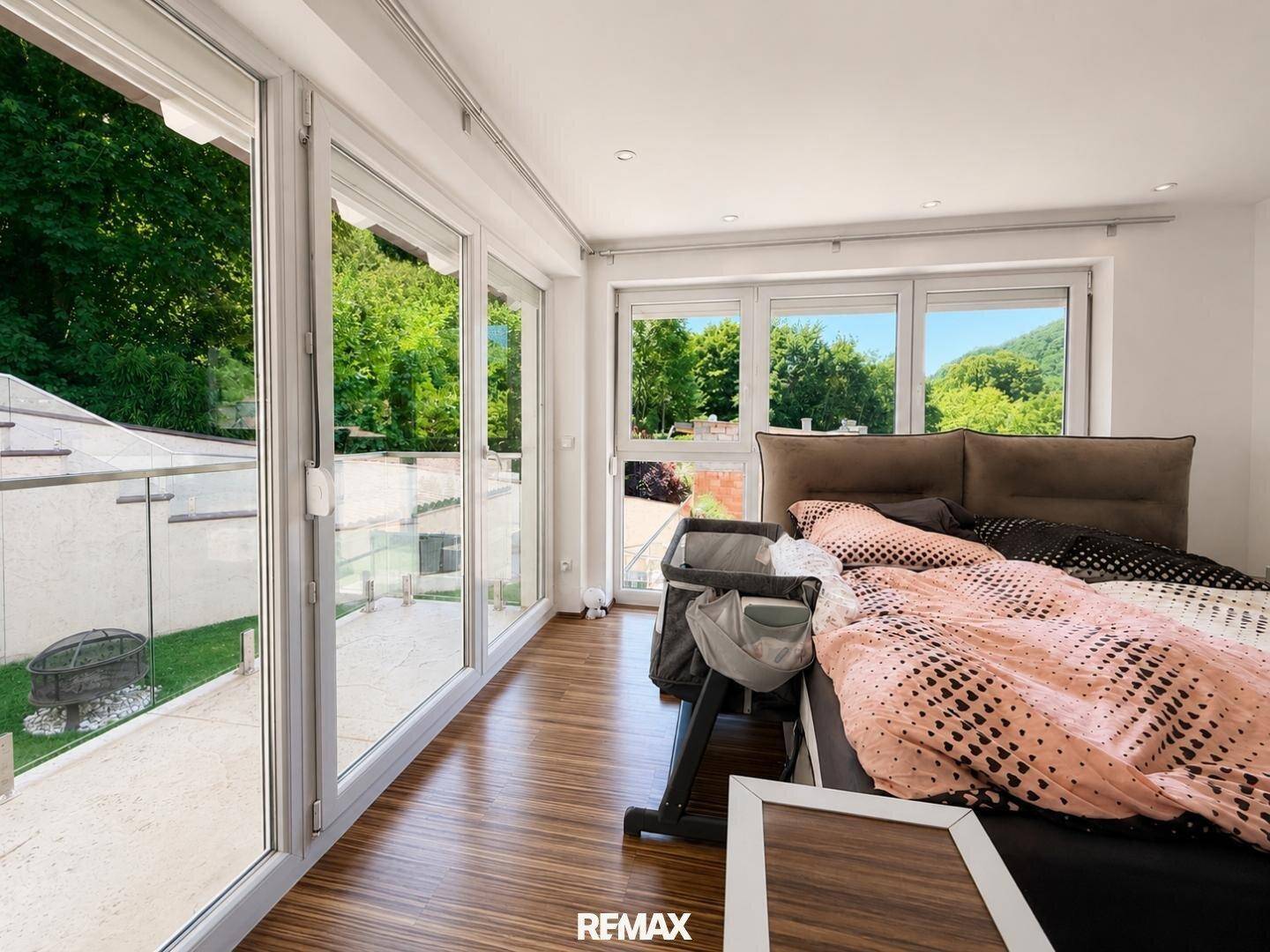 Schlafzimmer mit großen Fenstern und Zugang zu einer Terrasse oder einem Gartenbereich.