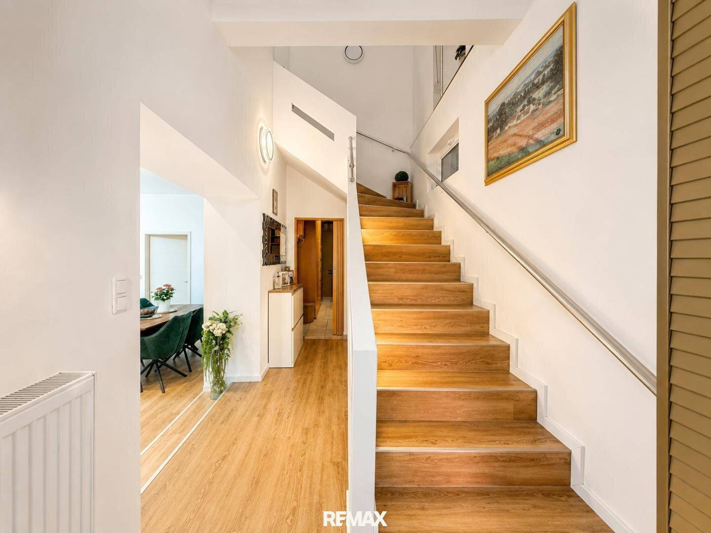 Geräumiger Flur mit Holztreppe und modernem Geländer, der zu den oberen Etagen führt.