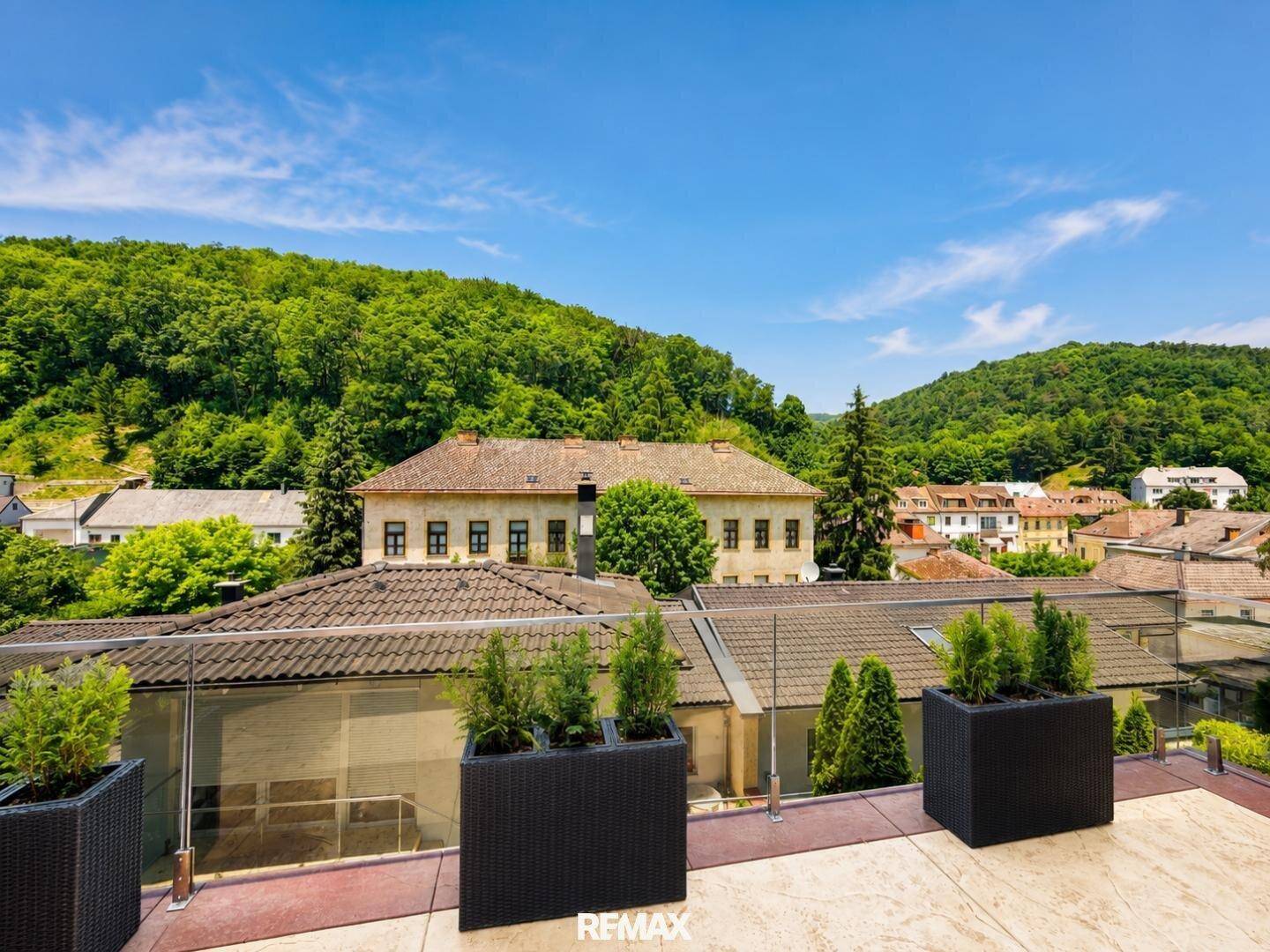 Weitläufiger Blick von der Terrasse auf die umliegende Wohnbebauung und bewaldete Hügel.