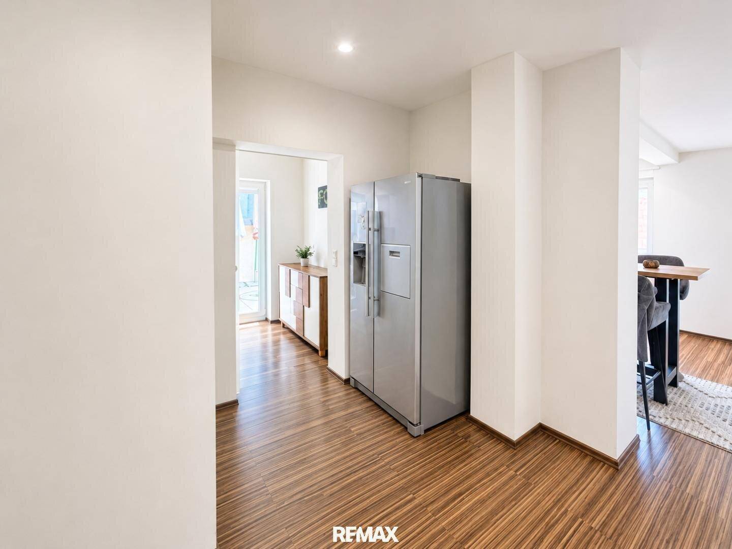 Heller Durchgangsbereich mit großem Kühlschrank und Holzboden, der zu anderen Räumen führt.