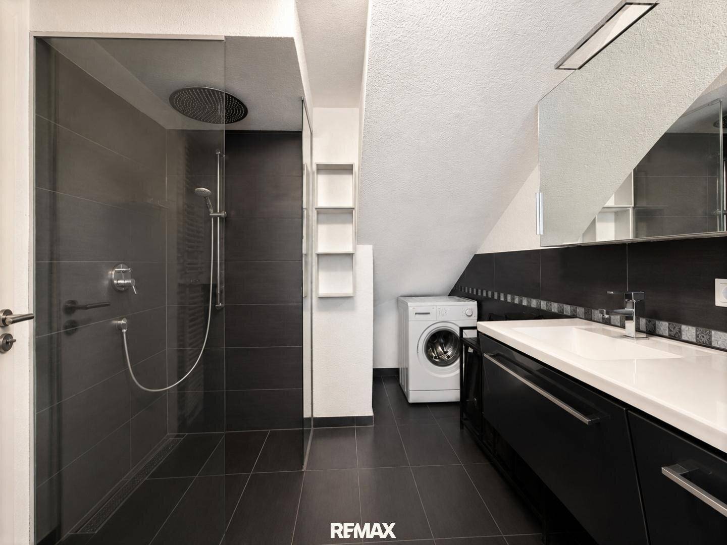 Badezimmer mit begehbarer Dusche, Waschbecken und Waschmaschine unter Dachschräge.