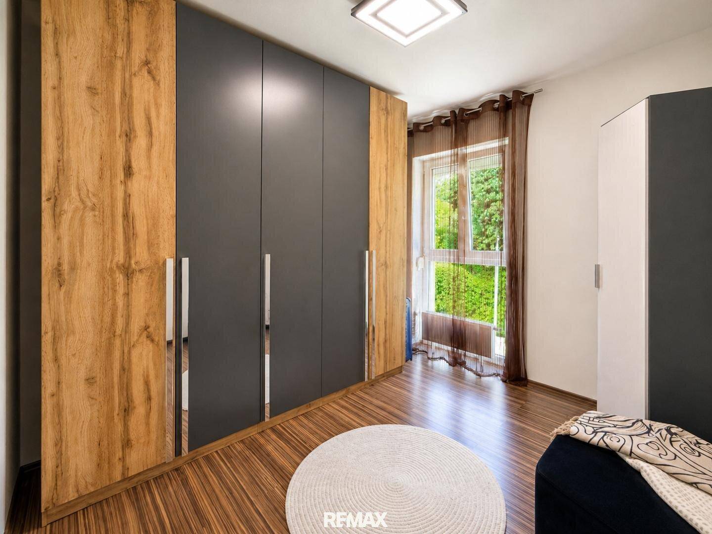 Schlafzimmer mit großem Kleiderschrank in Holz- und Anthrazitoptik und Fenster.